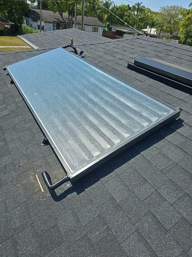 Residential solar hot water collector panel installed on a dark shingle roof for domestic water heating.