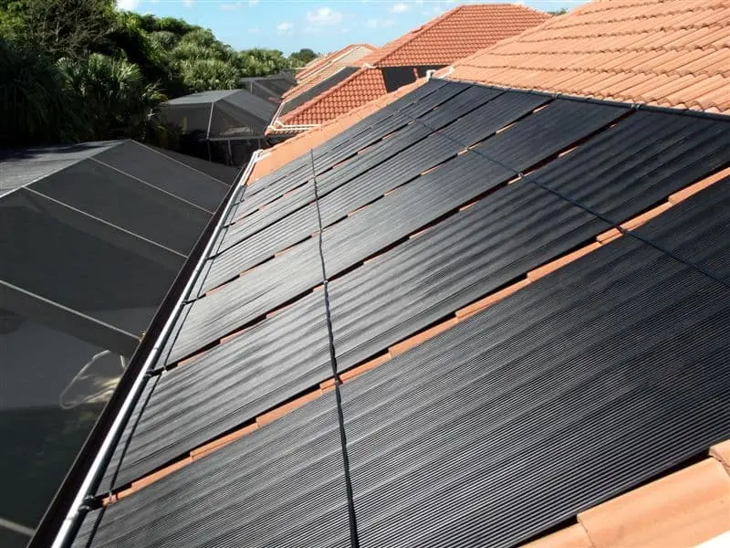 Residential solar pool heating system mounted on a terracotta tile roof for energy-efficient swimming pool temperature control.